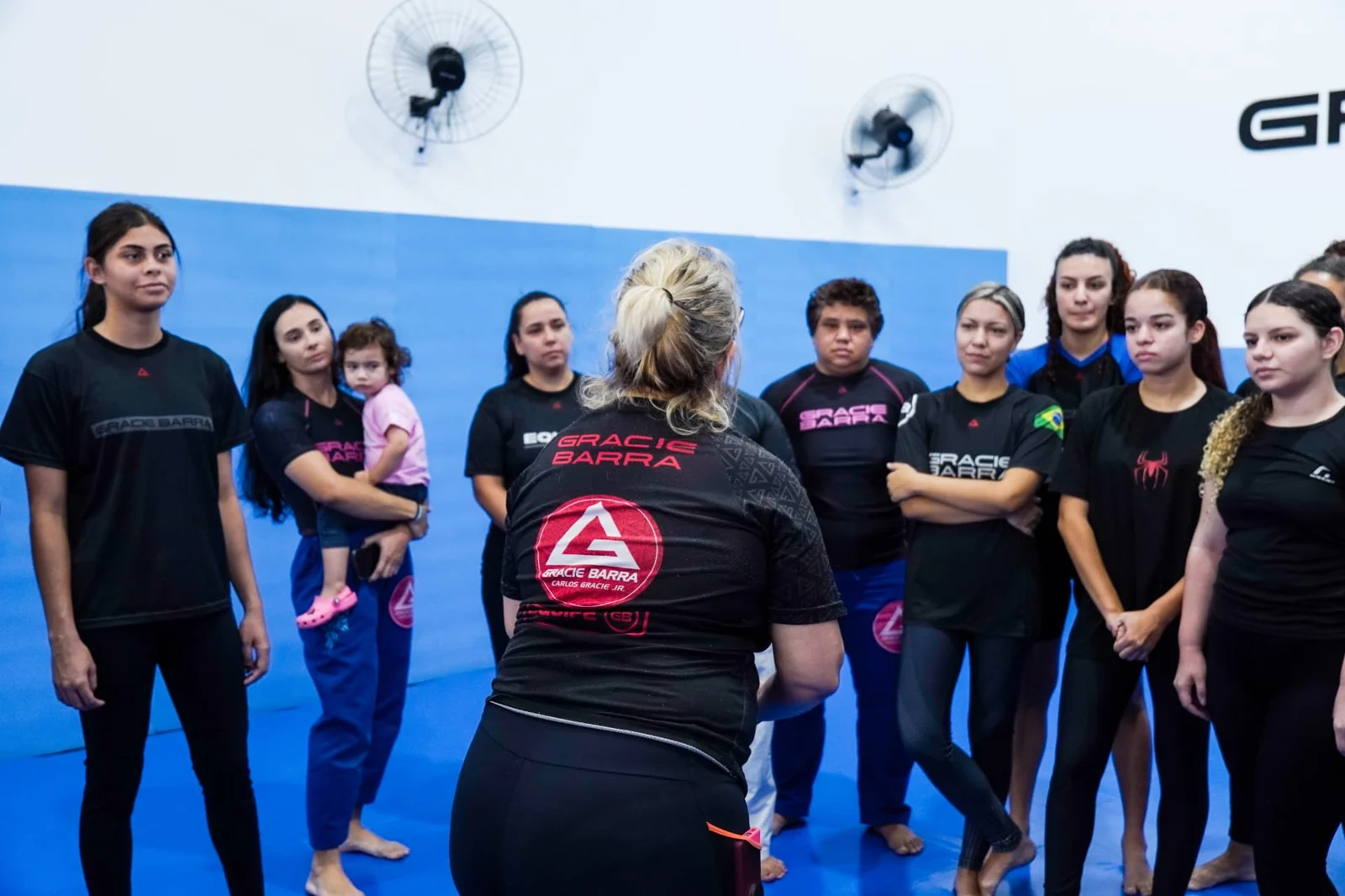 Mulheres reunidas no tatame ouvindo a Profª Carla